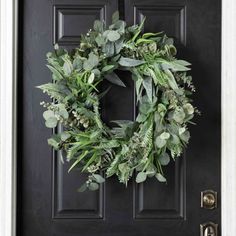 a wreath on the front door of a house with greenery hanging from it's side