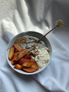 a white bowl filled with food on top of a white cloth covered table next to a metal spoon