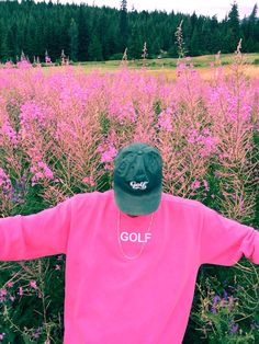 a person in a pink shirt and green hat standing in a field with purple flowers