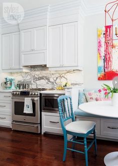 a kitchen with white cabinets and blue chairs next to a stove top oven in the center