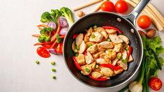 a pan filled with chicken and veggies next to chopsticks on top of a table