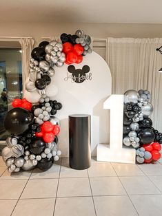 the balloon arch is decorated with black, silver and red balloons for a mickey mouse 1st birthday party