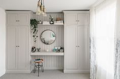 a room with white cabinets and a round mirror on the wall next to a stool