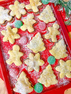 a red tray filled with christmas cookies on top of a wooden table covered in powdered sugar