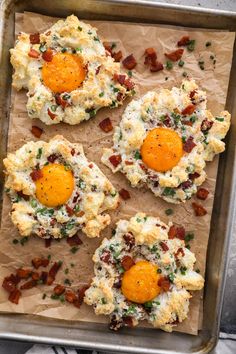 four biscuits with eggs and bacon in them on a baking sheet, ready to go into the oven