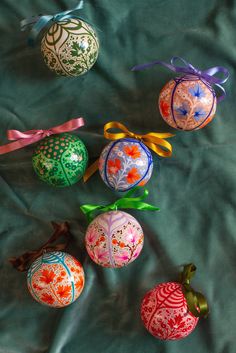 six decorated eggs with ribbons on a green cloth background, one has an ornament and the other has a bow