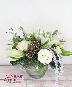 a glass vase filled with white flowers and pine cones