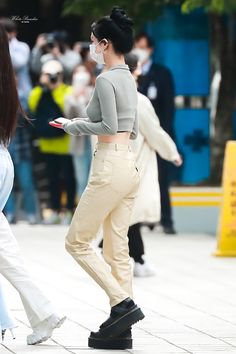 a woman in grey shirt and white pants standing next to another woman with black hair