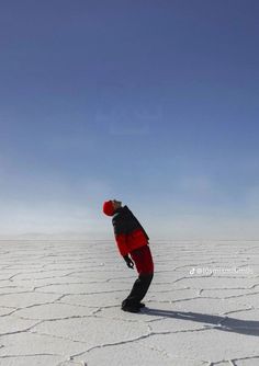 a man standing on top of a snow covered ground next to a blue sky in the middle of nowhere