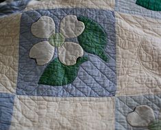 a quilted bed with white flowers and green leaves on the top, in front of a black background