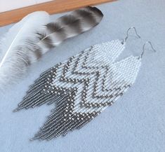 a feather and some beads on a blue rug next to a pair of silver earrings