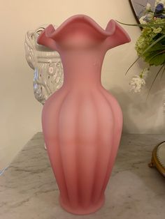 a pink vase sitting on top of a marble table next to a mirror and flowers