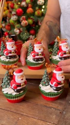 santa clause cupcakes are being held by someone's hand in front of a christmas tree