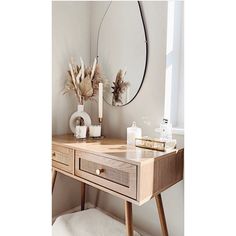 a wooden desk topped with a mirror next to a vase filled with dried flowers and candles