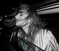 a woman sitting in the back seat of a car with her hair blowing in the wind