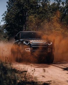 a black truck driving down a dirt road next to some tall grass and tree's