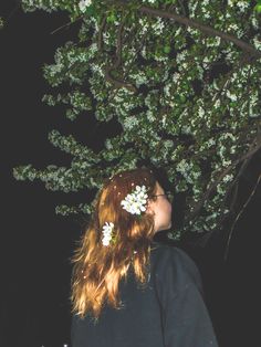 a woman standing under a tree with flowers in her hair and looking up at the sky