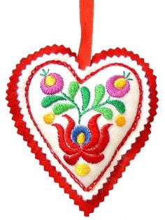 an ornament shaped like a heart with flowers on the front and bottom, hanging from a red ribbon