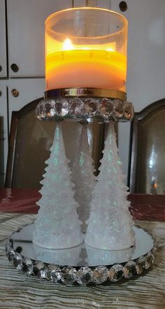 a candle is sitting on top of a glass plate with snow covered trees in it