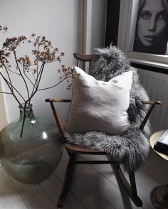 a chair sitting next to a vase with flowers in it and a pillow on the floor