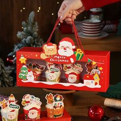 a person is holding a christmas cupcake box with santa's decorations on it