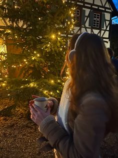 a woman standing in front of a christmas tree holding a cup