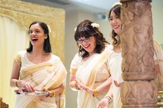 two women in saris are laughing and holding plates with food on them while another woman looks on