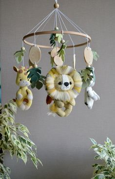 a baby mobile with stuffed animals hanging from it's sides in front of a potted plant