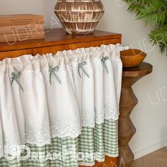 a close up of a window curtain on a table with a plant in the background