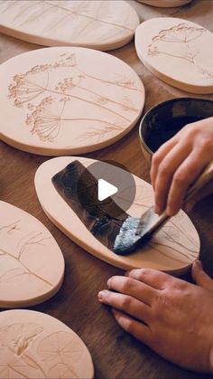 a person is using a brush to paint flowers on wooden plates with wood engravings