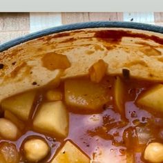 a bowl filled with stew and potatoes on top of a wooden table next to a spoon