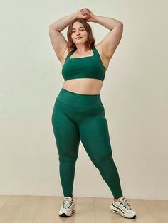 a woman in green sports bra and leggings poses for the camera with her hands behind her head