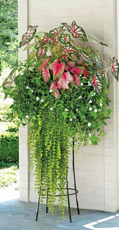 a tall planter filled with lots of green and pink flowers sitting on top of a metal stand