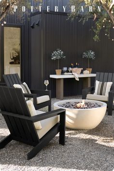 an outdoor fire pit surrounded by chairs and tables with potted trees in the background