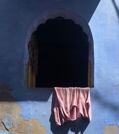 a pink towel hanging from the side of a blue building with an arched window and door