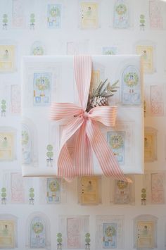 a gift wrapped in white paper with a pink bow on it's side, sitting against a wallpapered background