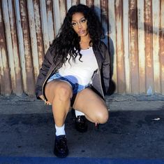 a woman sitting on the ground with her legs crossed and wearing short shorts, white shirt and black boots