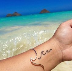 a person with a tattoo on their arm holding a cell phone in front of the ocean