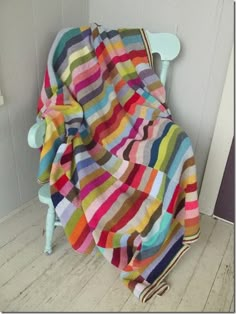 a multicolored blanket sitting on top of a wooden chair next to a wall