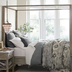 a bed sitting under a window next to a table with a lamp on top of it