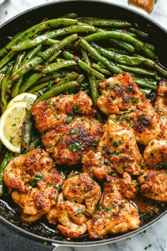 chicken and green beans in a skillet with lemon wedges on the side for garnish