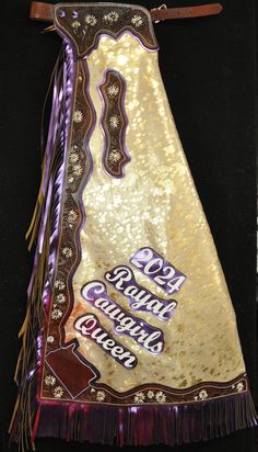 a gold and purple bag with fringes on it's sides, hanging from a black wall