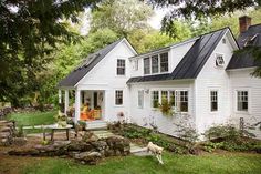 a white house with black shingles and lots of windows on the front door is surrounded by greenery