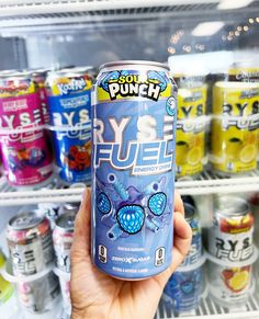 a person holding up a can of soda in front of a refrigerator full of drinks