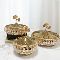 two golden dishes sitting on top of a white table next to a black tray with gold decorations