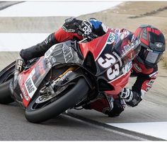 a man riding on the back of a red motorcycle down a race track in front of another person