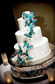 a white wedding cake with blue butterflies on top and candles in the background for decoration