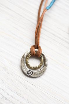 DharmaShop founder, Sander Cohen, purchased this necklace for himself on his trip to Nepal in 2018. He and everyone at our office loved it so much that we knew we had to carry it! The stylish hand hammered brass and silver double ring pendant has two sides. Written on one is the word, "Happiness" in Sanskrit script. The other side features a small hand etched smiley face. Pendant is hand strung on dark brown faux suede cord with a blue accent and sliding wood bead closure for adjustable length. Adjustable Hand Stamped Metal Necklace, Spiritual Hammered Adjustable Necklace, Hammered Spiritual Necklaces With Adjustable Fit, Adjustable Hammered Spiritual Necklaces, Adjustable Brass Necklace With Hammered Detail, Adjustable Everyday Necklace With Oxidized Finish, Adjustable Necklace With Oxidized Finish For Everyday, Everyday Adjustable Necklaces With Oxidized Finish, Everyday Nickel Free Metal Necklace