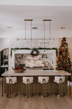 a kitchen decorated for christmas with white stools and a tree in the center area