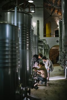 three men are working on something in a large room filled with metal pipes and tanks